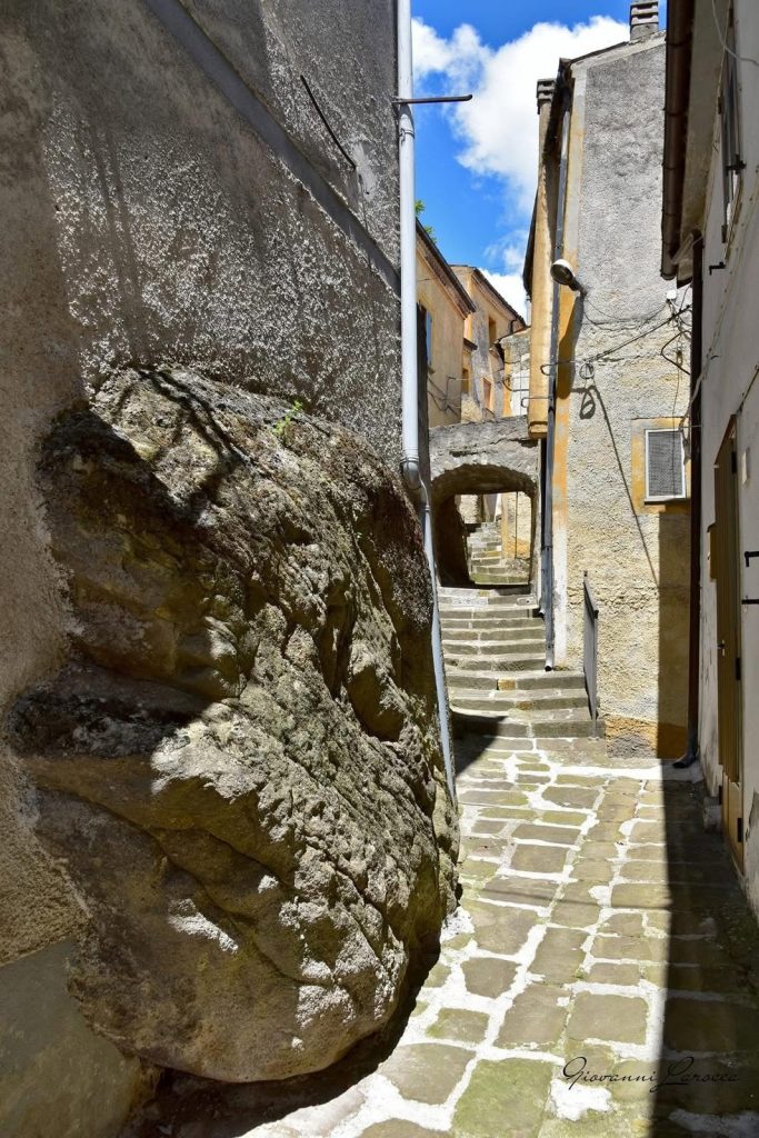 Vicolo lastricato con grande roccia e scalinata sotto un arco, centro storico di Calvello