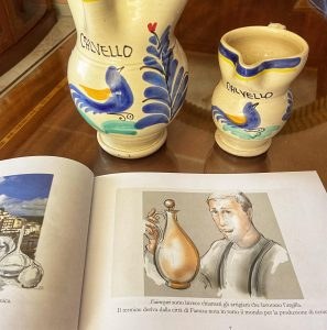 Due brocche calvellesi con l’uccellino accanto a un libro aperto sulla storia dei Faenzari