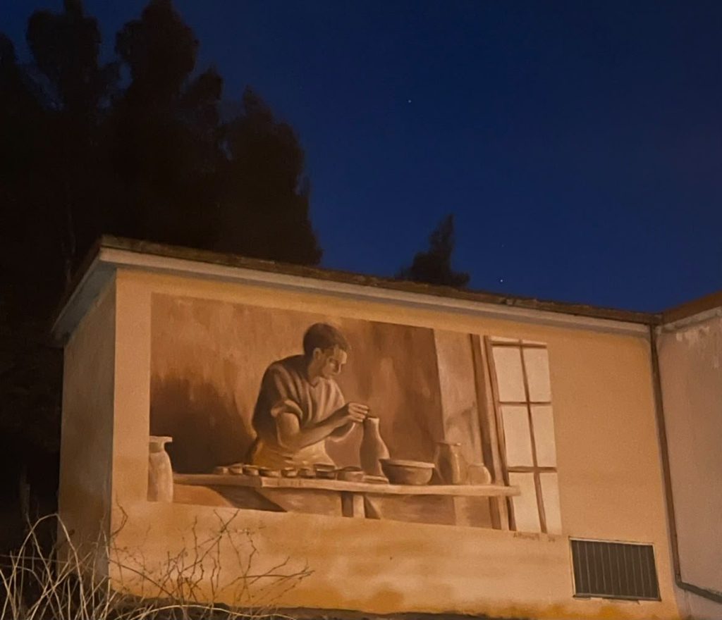 Murale nei toni della terracotta con un vasaio al lavoro tra brocche e ciotole
