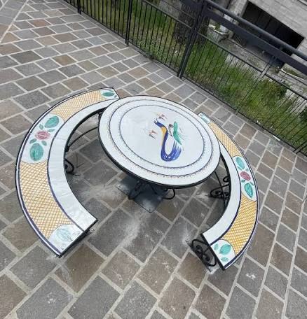 Tavolo rotondo e panche curve rivestiti di maiolica con l’uccellino e decori floreali